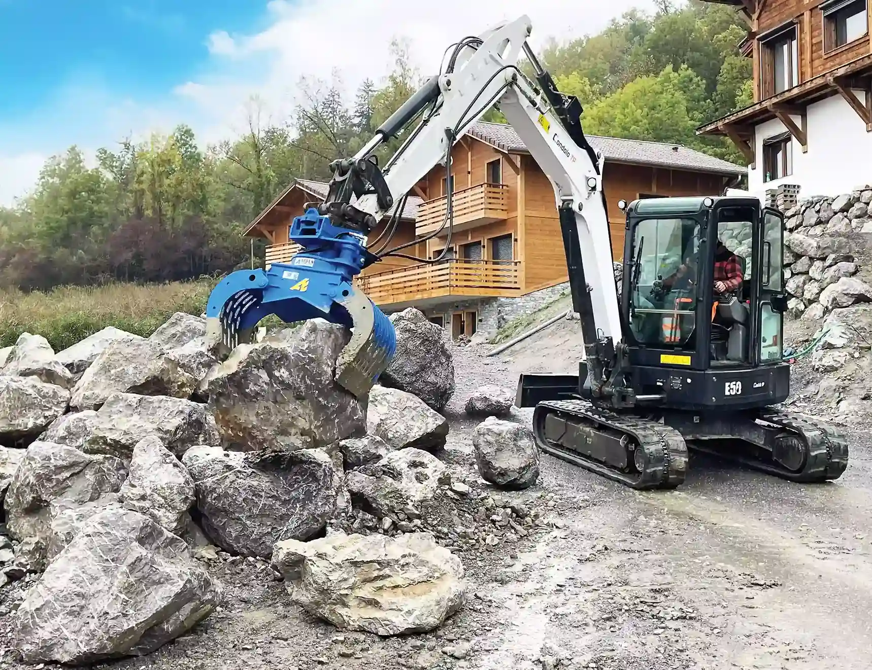 Mini-excavadora equipada con una pinza vers&aacute;til Mini-Blue de Arden Equipment, manipulando grandes bloques de piedra en obra, ideal para trabajos de manejo y recuperaci&oacute;n.